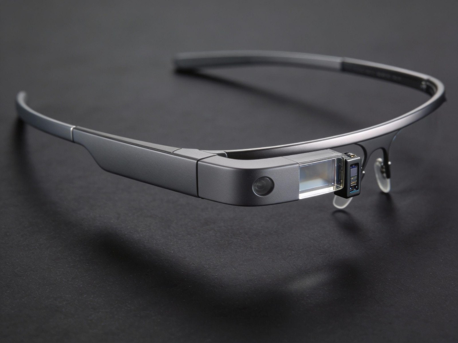 A pair of Google Glass smart glasses on a dark surface, showing the slim head-mounted frame and the prism display module that projects content into the wearer's field of view.